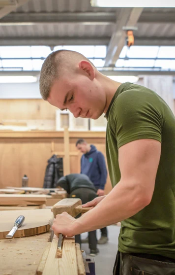 A joinery student focused on chiseling wood, using a mallet at a workbench during practical training in a woodworking class. A joinery student focused on chiseling wood, using a mallet at a workbench during practical training in a woodworking class.